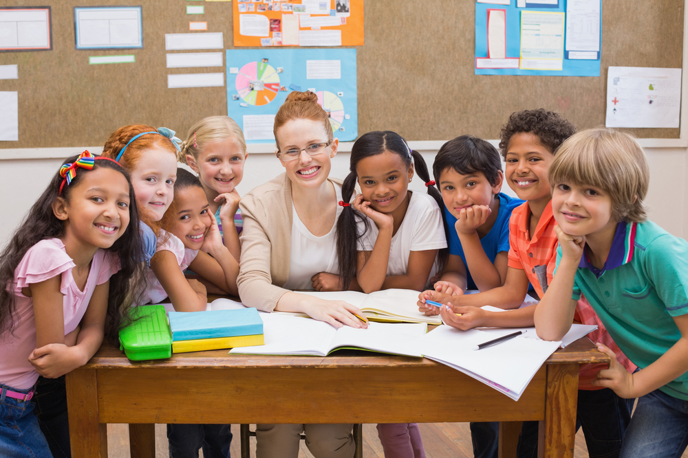 Teacher and pupils working at desk together at the elementary school